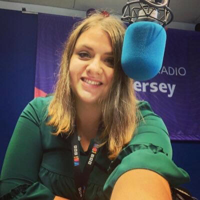 A smiling woman in a green dress sits behind a BBC branded microphone.